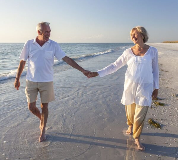 Financial Adviser Perth - Happy older couple walking on beach holding hands showing freedom and retirement confidence